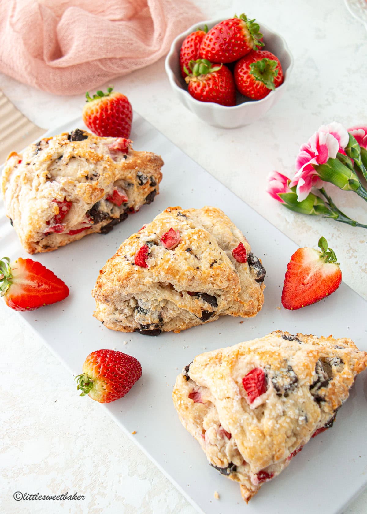 Three strawberry chocolate scones on a white porcelain serving board.