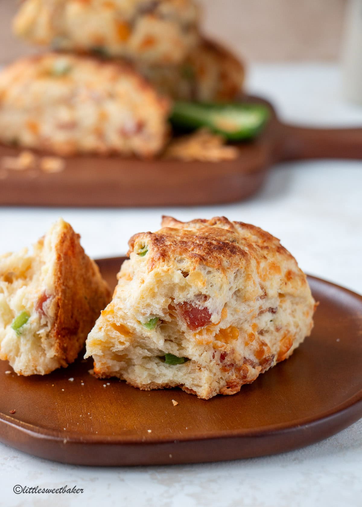 A bacon cheddar scone broken in half on a small wooden plate.