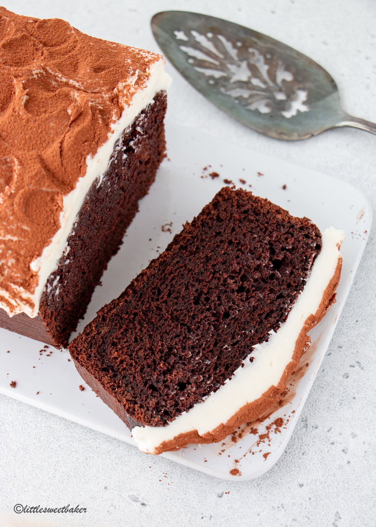 A loaf of chocolate Guinness cake on white serving board with a slice cut.