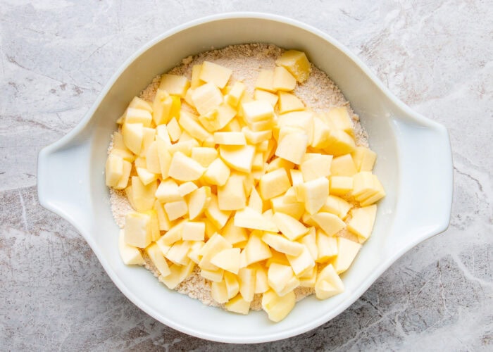 A bowl of chopped apple on top of the dry ingredients for Irish apple cake.