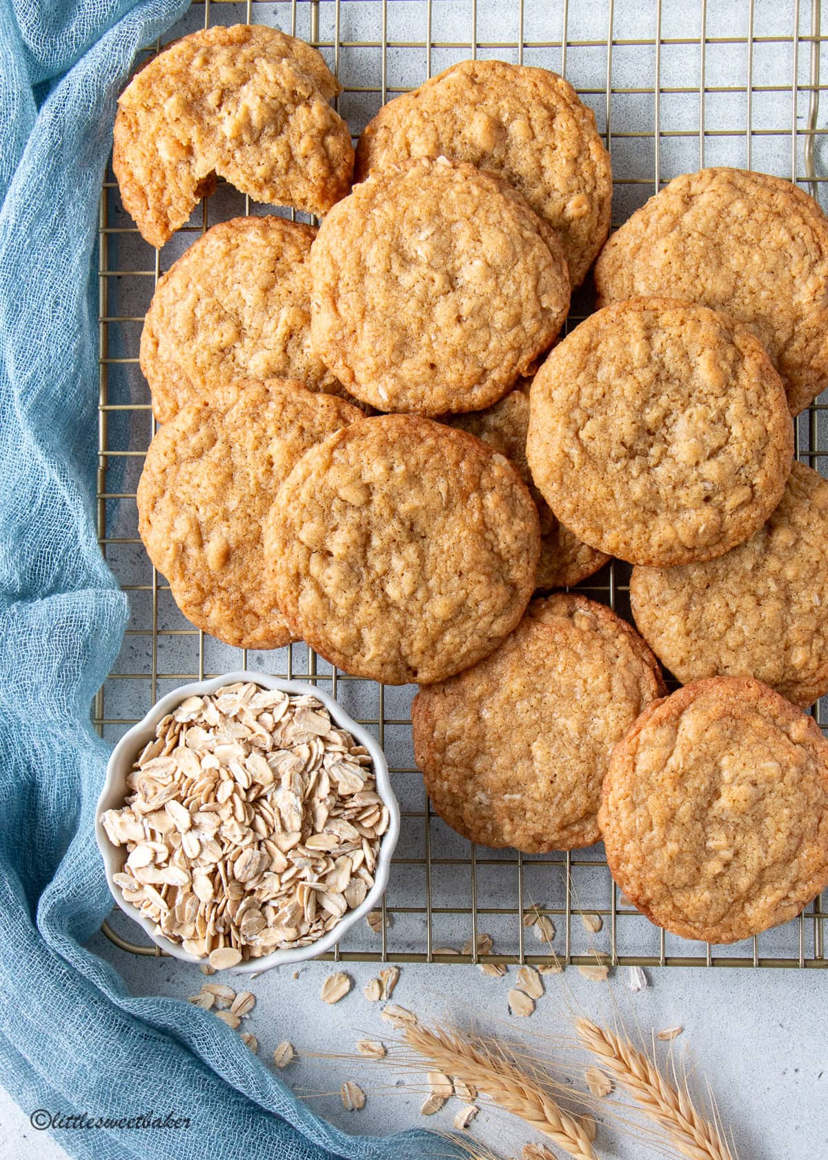 Chewy coconut oatmeal cookies piled on a cooling rack with a bowl of rolled oats and blue chiffon napkin.