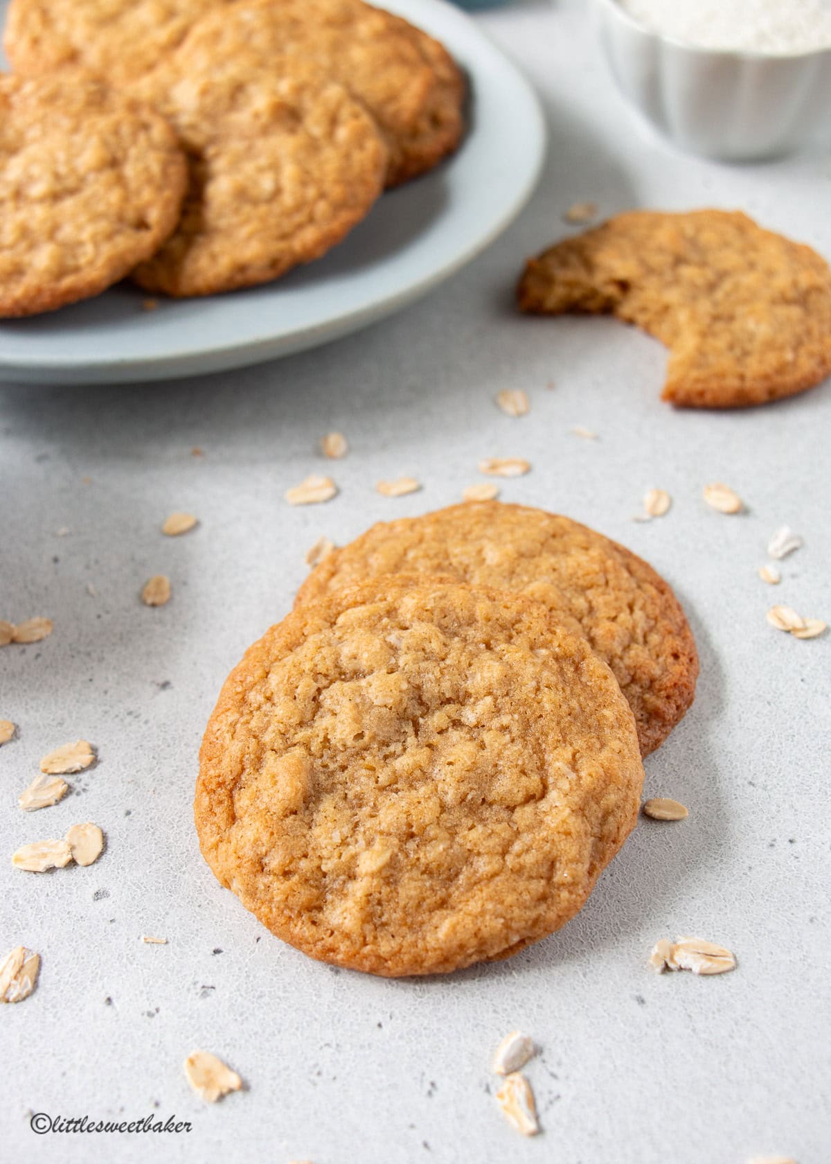Two coconut oatmeal cookies overlapping with a plate of cookies in the background.