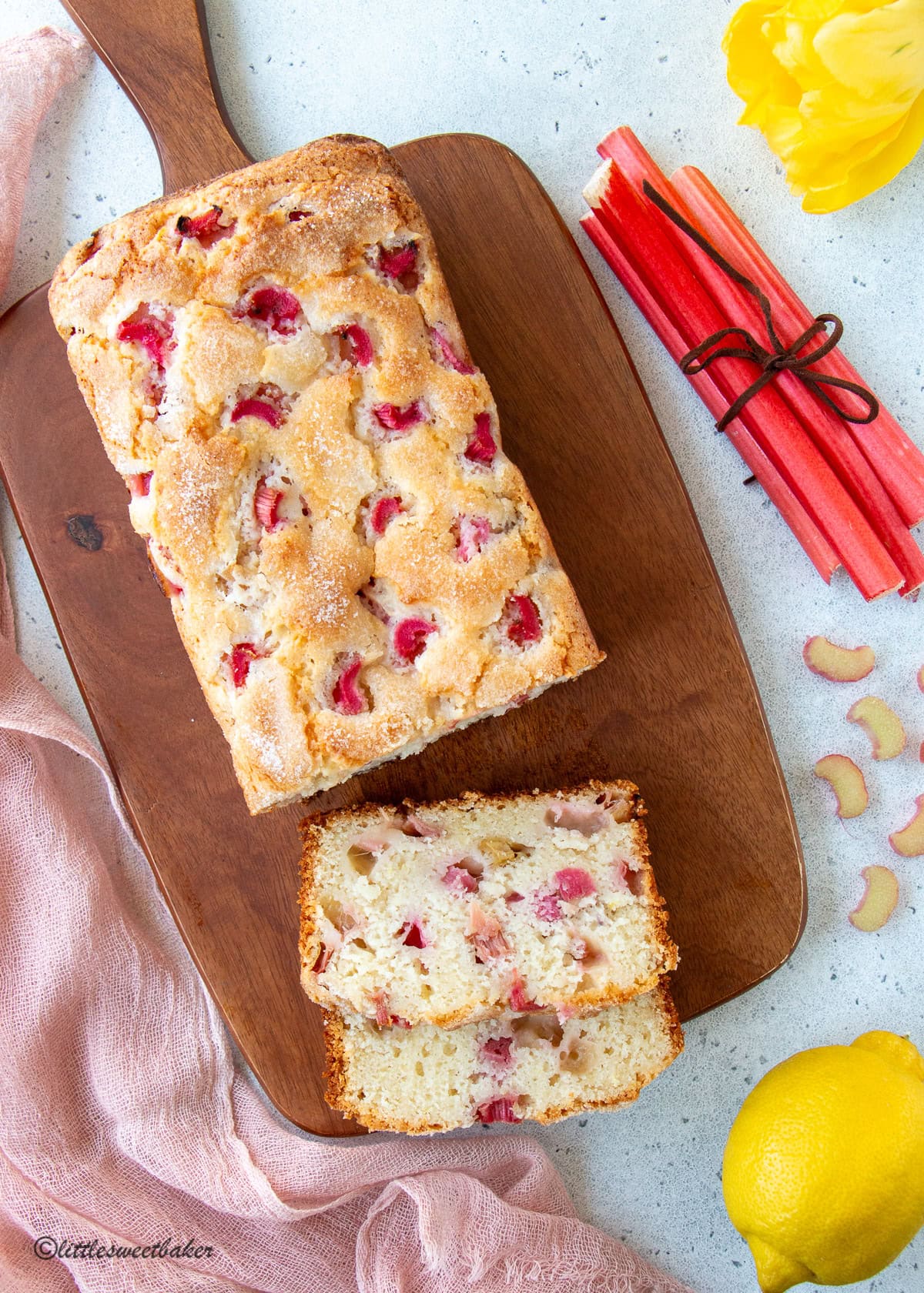 An overhead view of a loaf lemon rhubarb bread on a wooden cutting board.