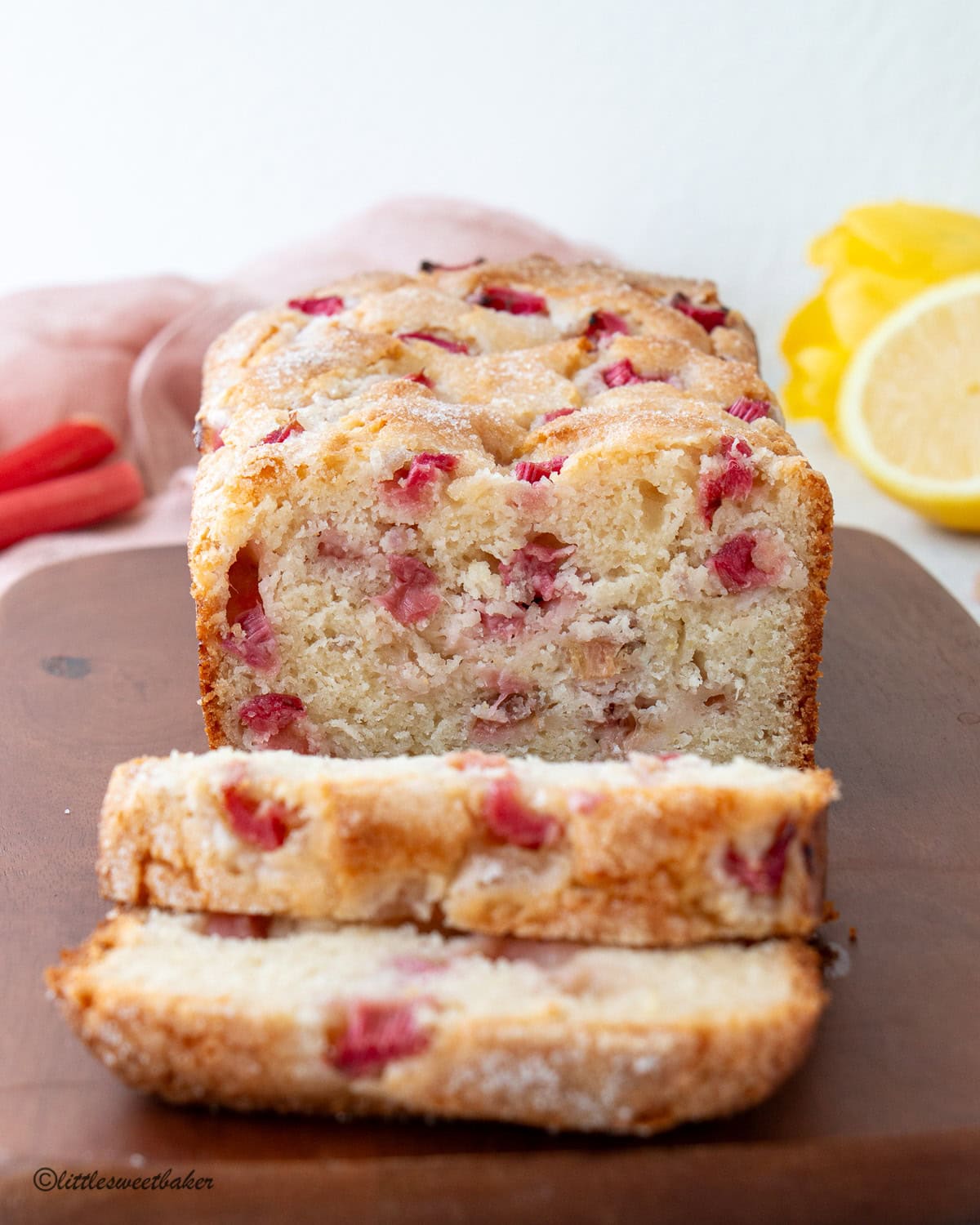 A lemon rhubarb loaf on a wooden cutting board with two slices cut.