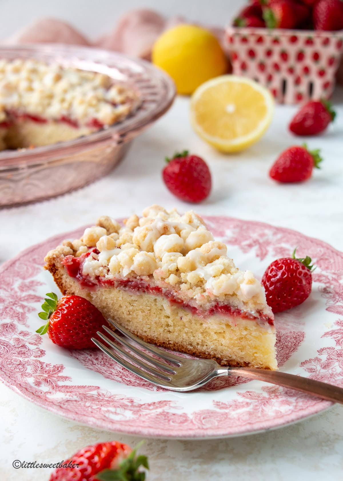 A slice of strawberry crumb cake on a pink plate with two strawberries.