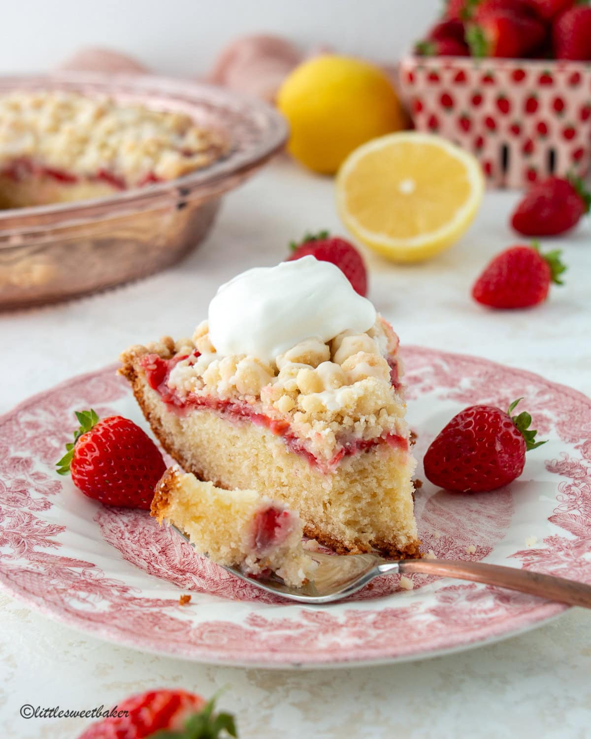 A slice of strawberry crumb cake topped with whipped cream on a pink plate with a piece on a fork.