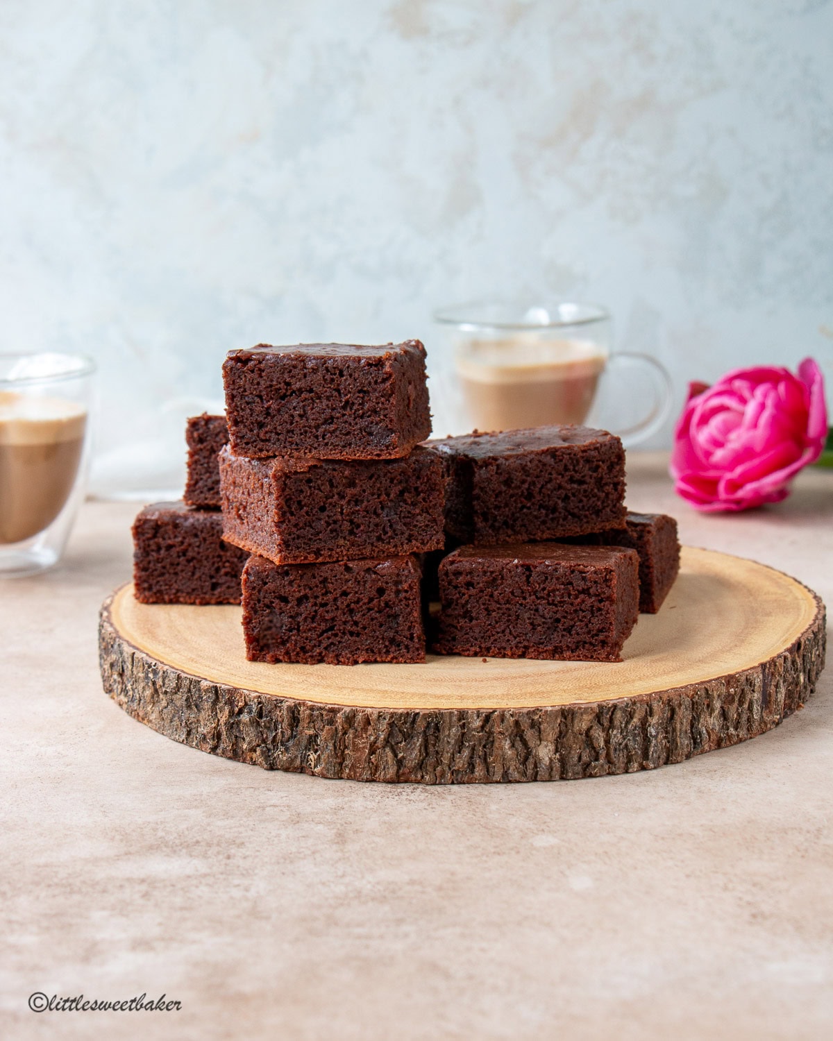 Mochi brownies on a live edge wooden board with a flower and two cappuccino in the background.