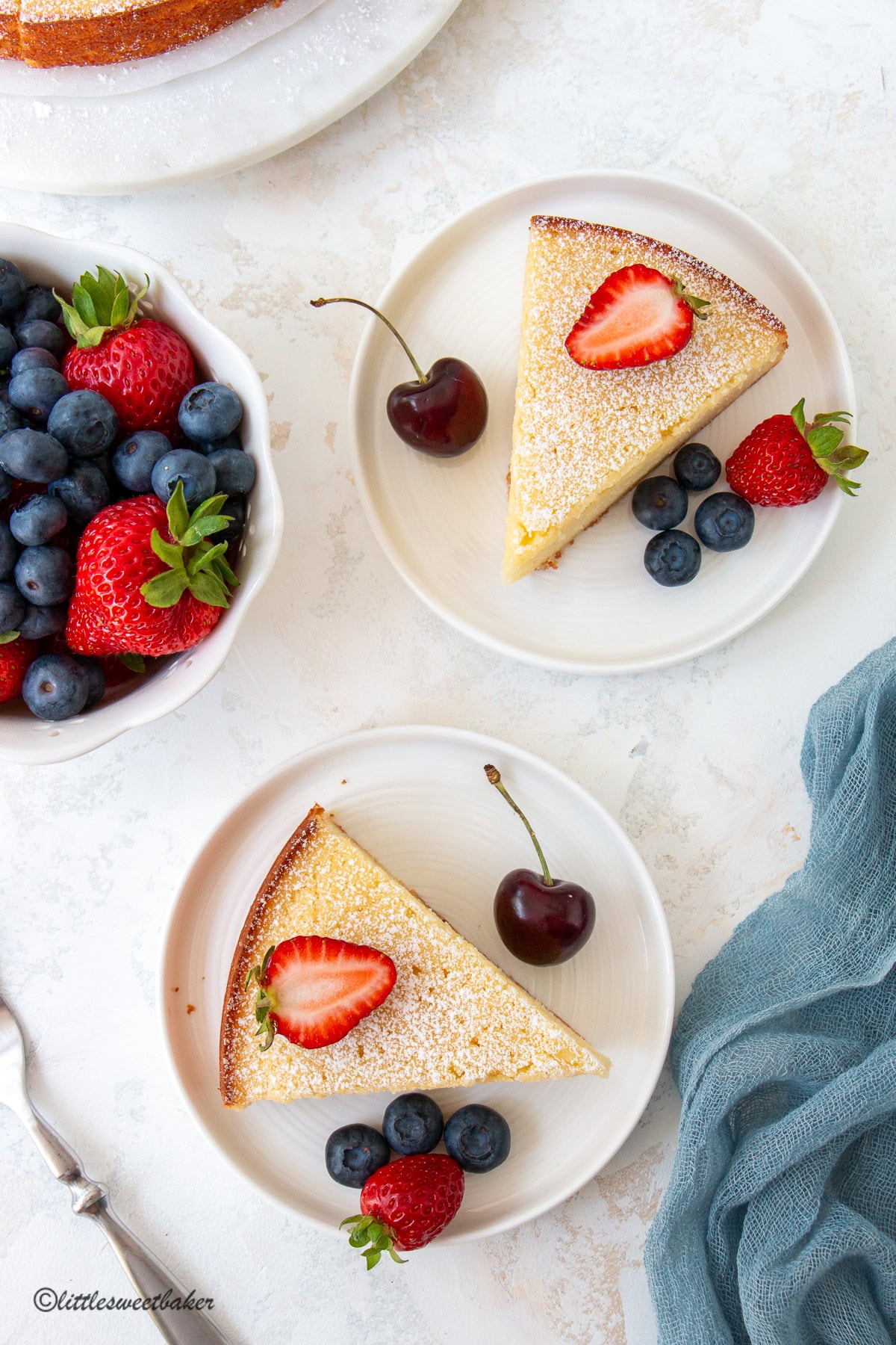 Overhead view of two slice of lemon ricotta cake on white plates with berries.