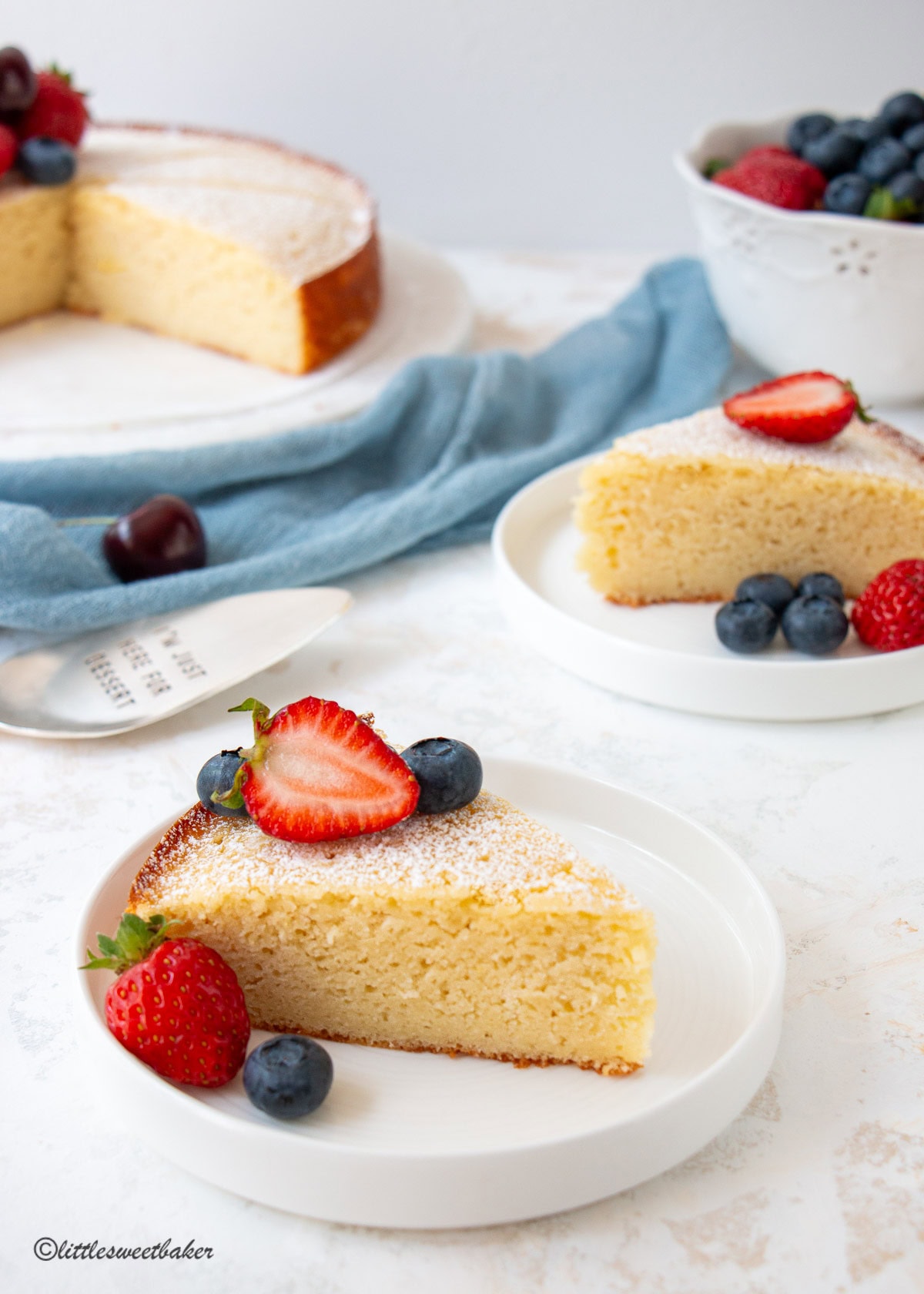 A slice of lemon ricotta cake on a white plate with strawberries and blueberries.