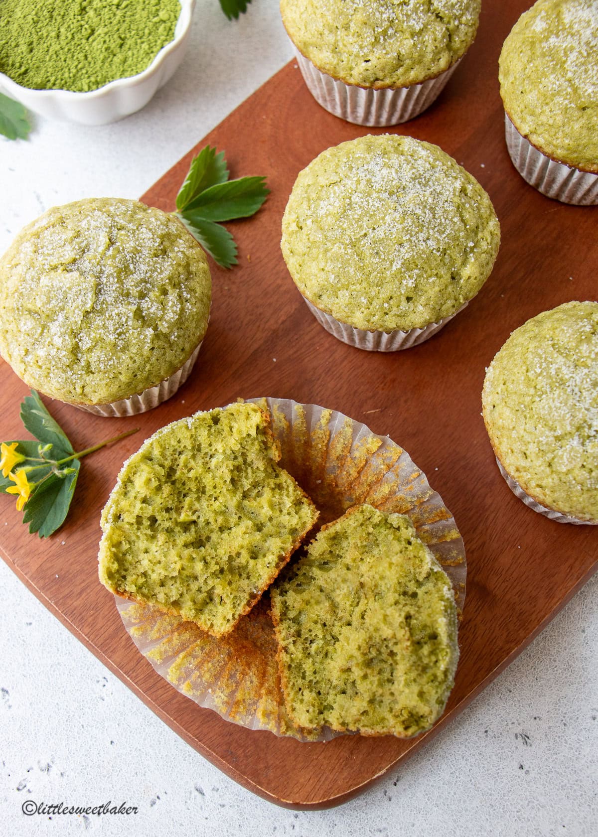 Matcha muffins on a wooden cutting board with one broken in half.
