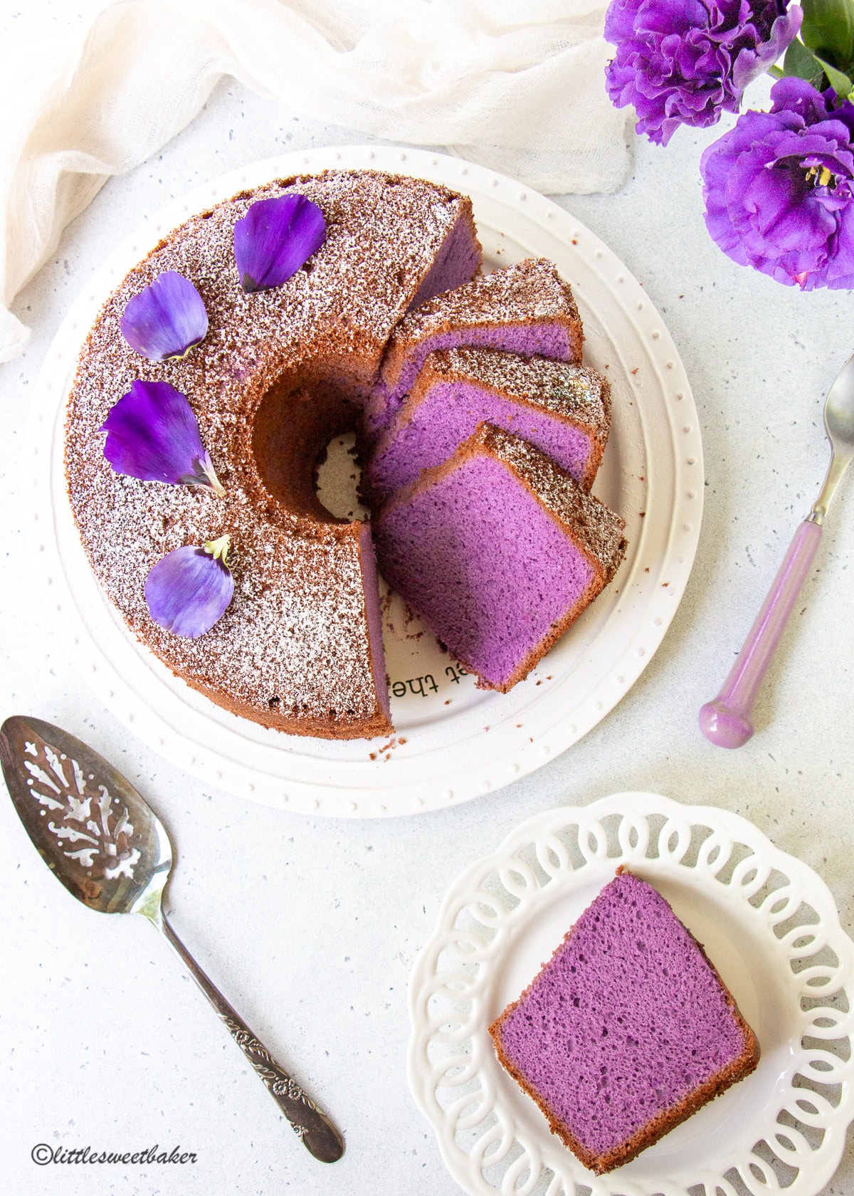 An overhead view of an ube chiffon cake topped with purple flower petals.