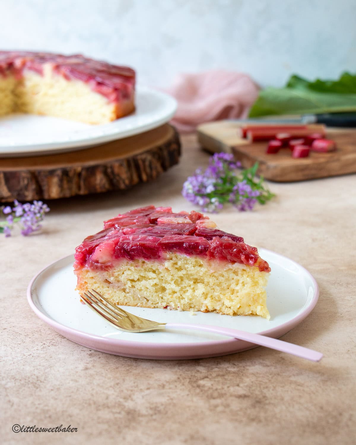 A slice of rhubarb upside-down cake on a white and pink plate with a pink and gold fork.