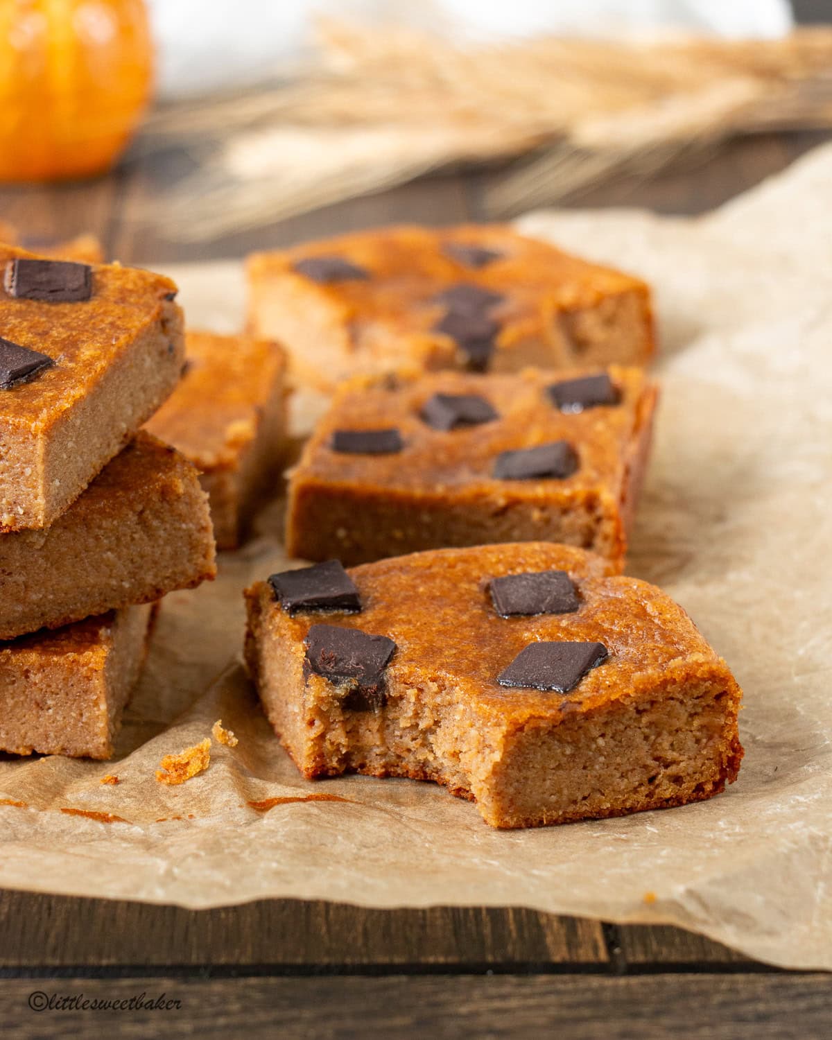 Healthy pumpkin bars with chocolate chunks on parchment with a bar with a bite taken out.