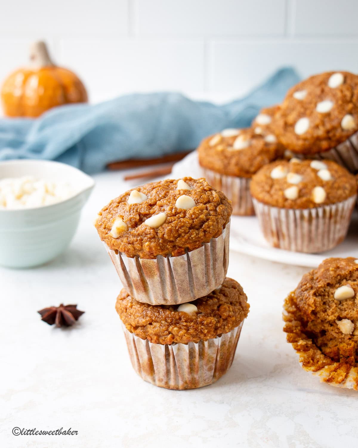 Two protein pumpkin muffins stacked with a plate of muffins in the background.