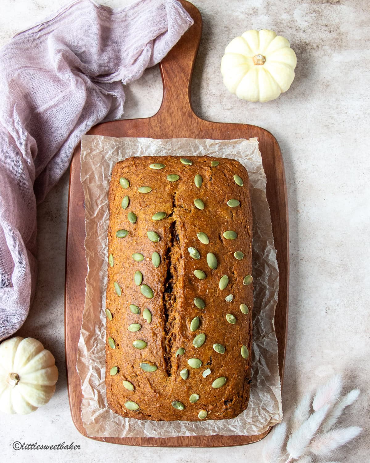 A loaf of healthy pumpkin bread on a wooden cutting board lined with parchment paper.