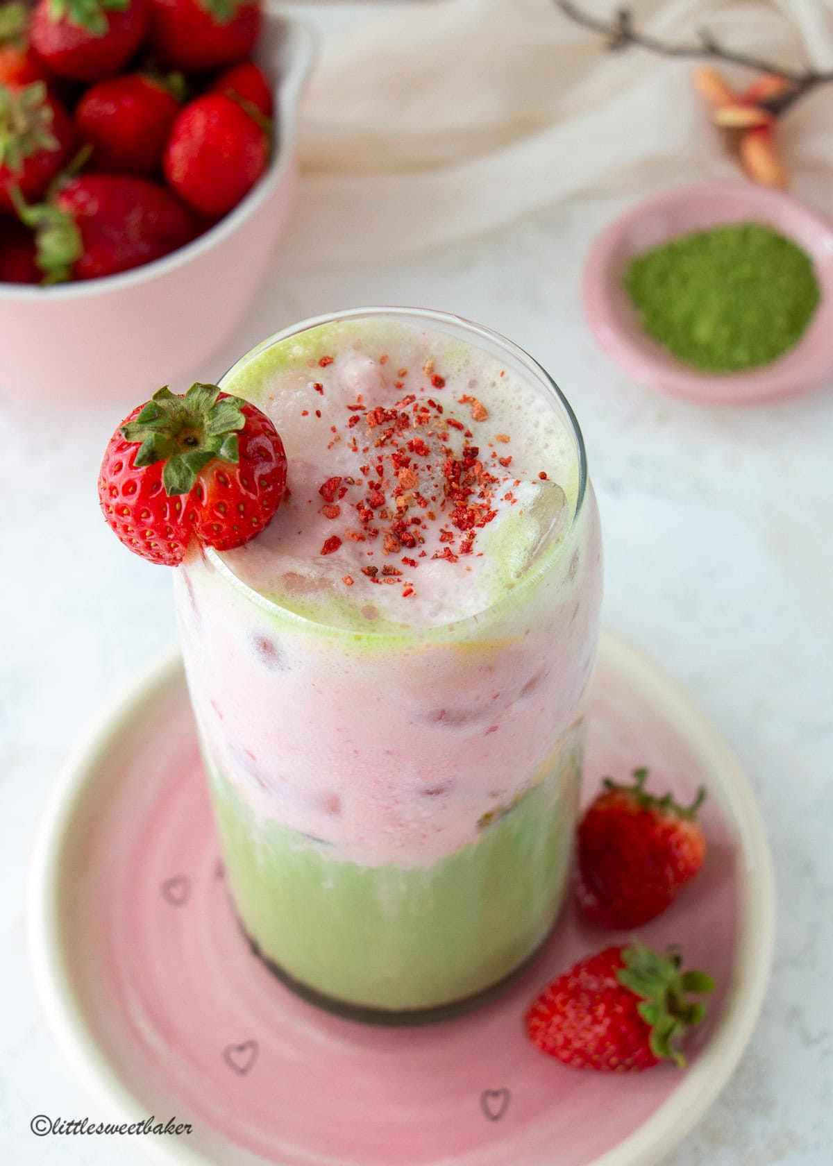 Strawberry protein cold foam matcha latte topped with crushed freeze-dried strawberries and a fresh strawberry.