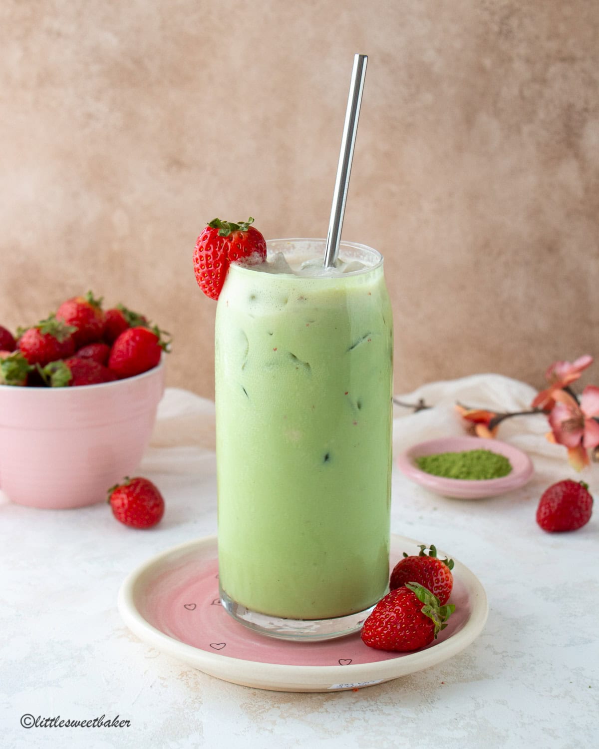 A glass of stirred strawberry protein cold foam matcha latte on a pink plate.