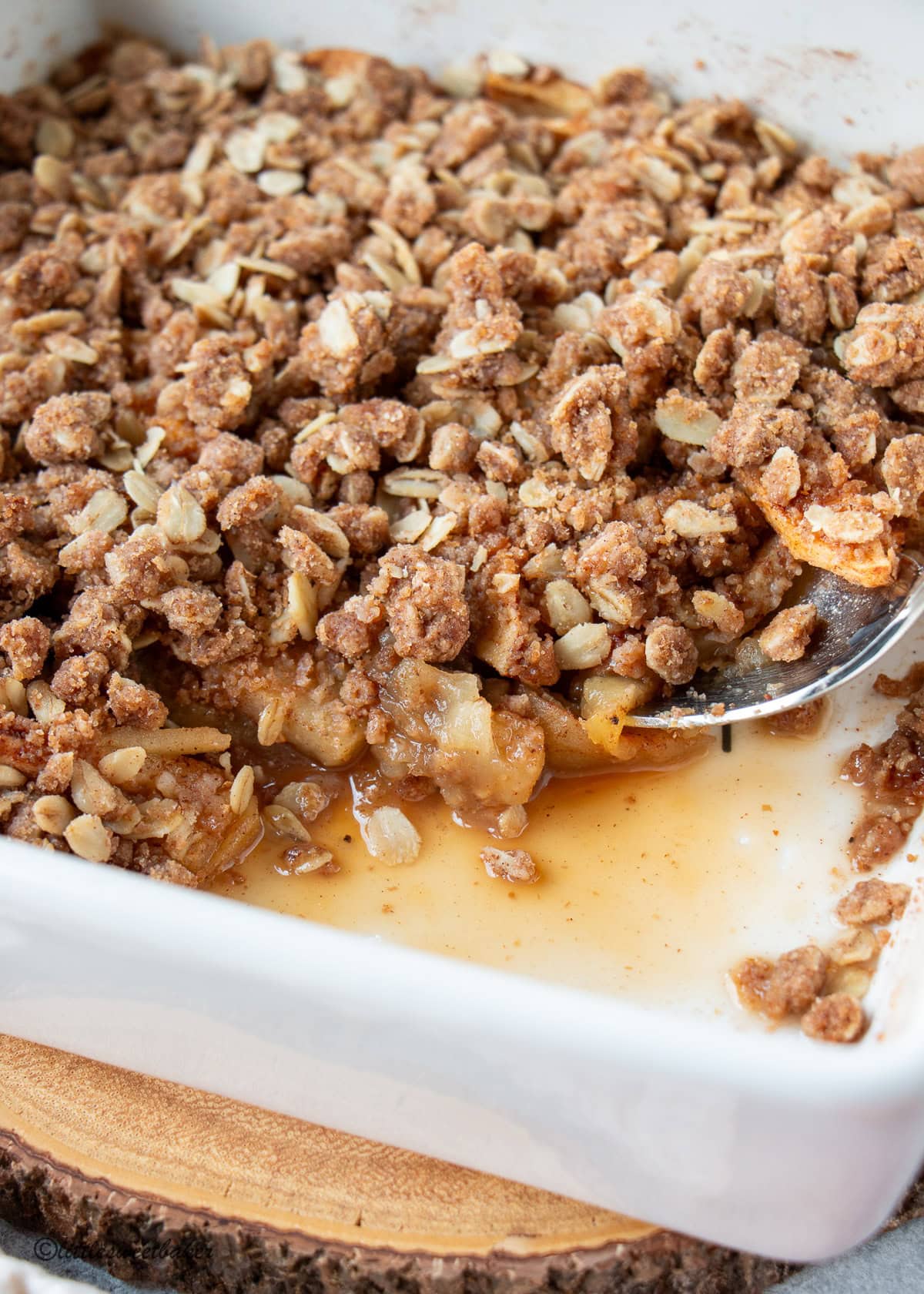 A close of healthy apple crisp in a white baking dish and serving spoon.