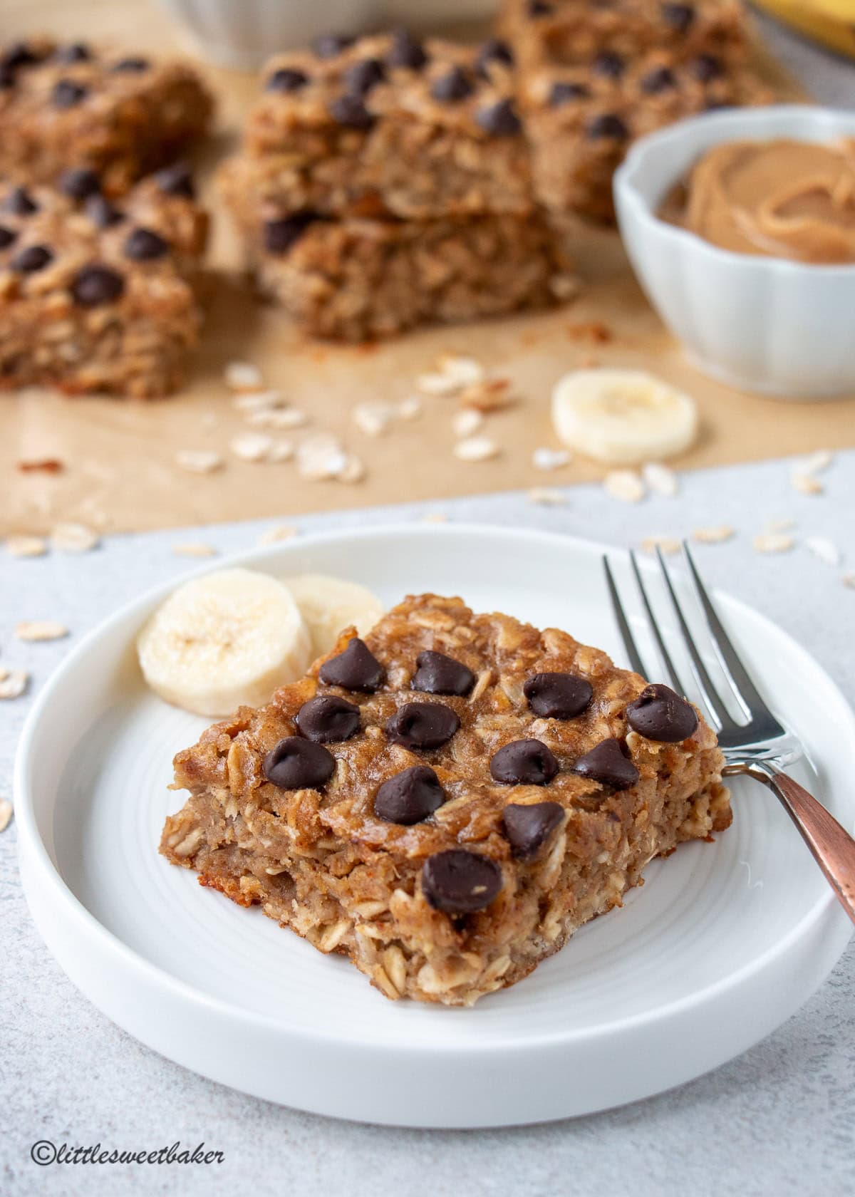 A Peanut Butter Banana Oatmeal Bar on a white plate with two slices of bananas and a fork.