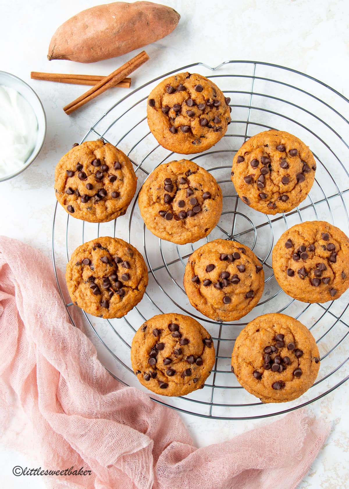 Healthy sweet potato muffins on a round cooling rack with a pink linen and sweet potato.