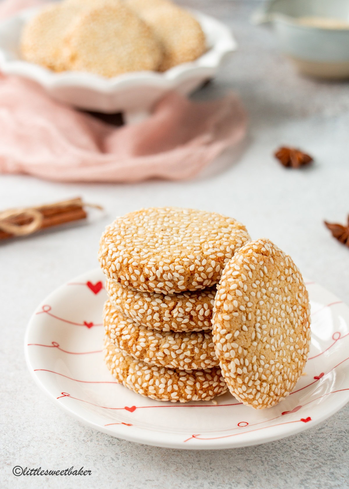 Honey sesame cookies stacked on a small white plate with hearts.