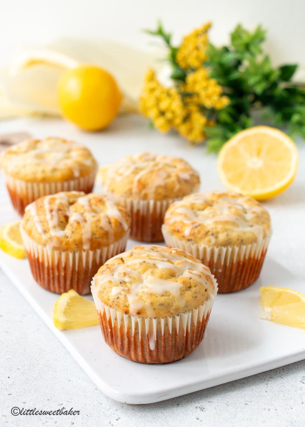 Five lemon chia seed muffins on a white porcelain cutting board.
