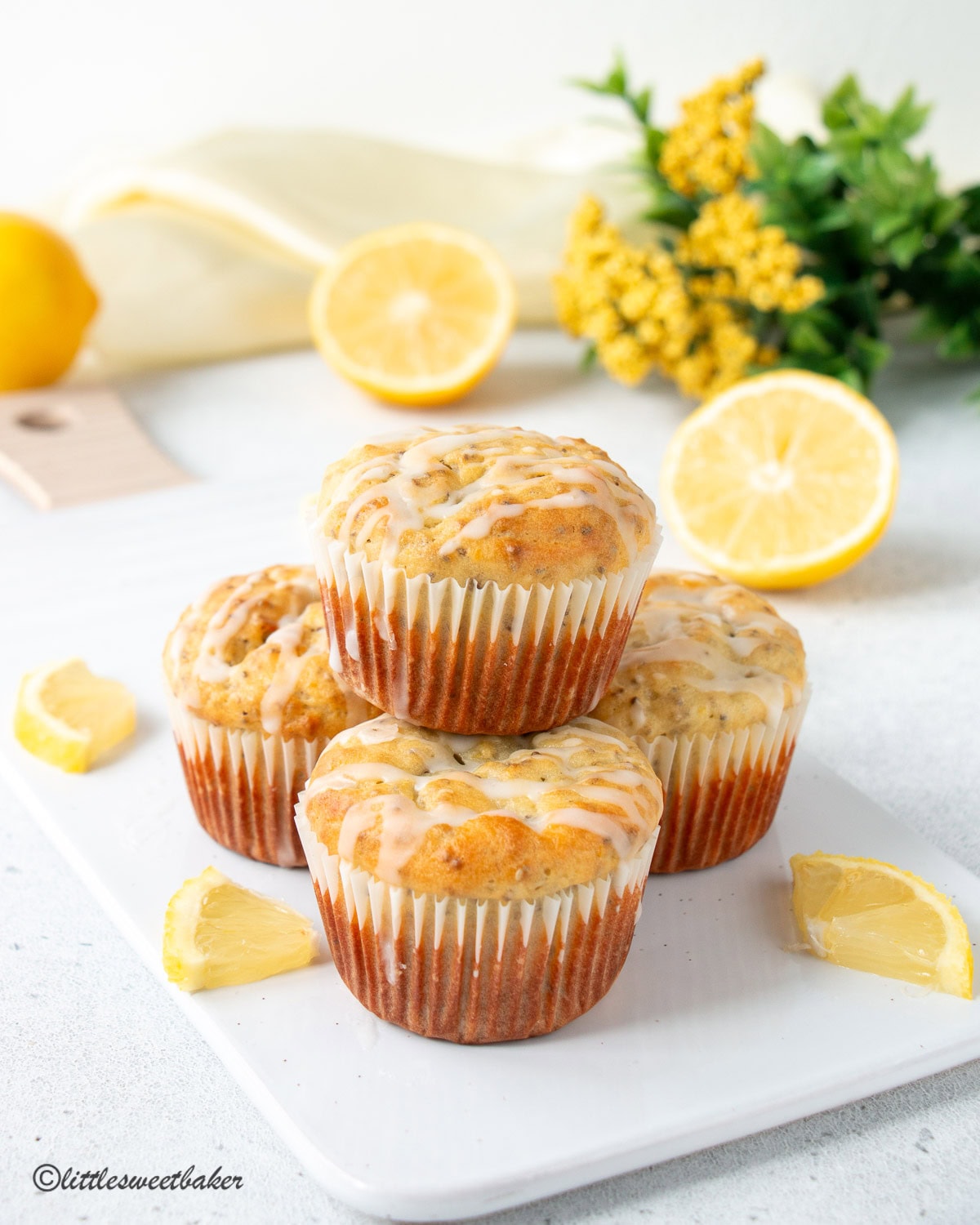Four Lemon Chia Seed Muffins, with the fourth stacked on top of the three, on a white porcelain cutting board.