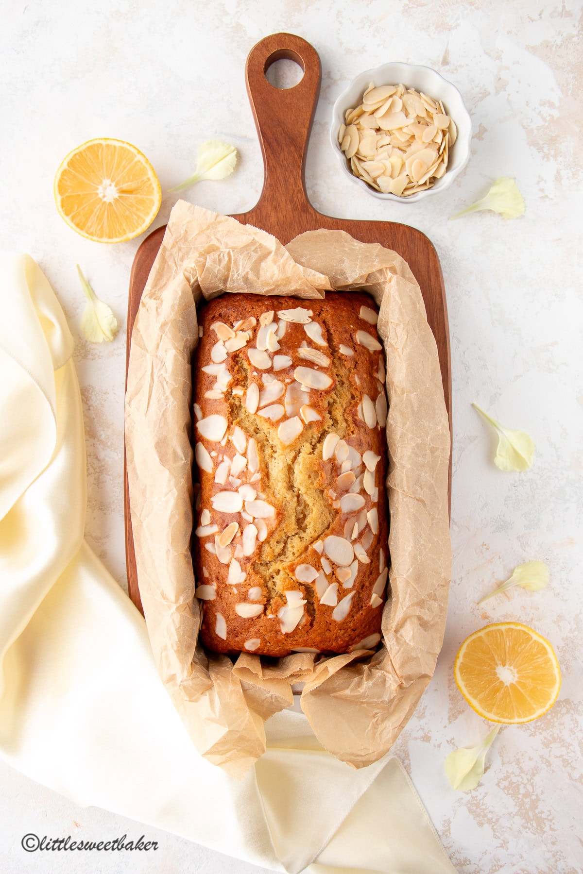 A loaf of healthy lemon cake in a pan lined with parchment paper on a cutting board.