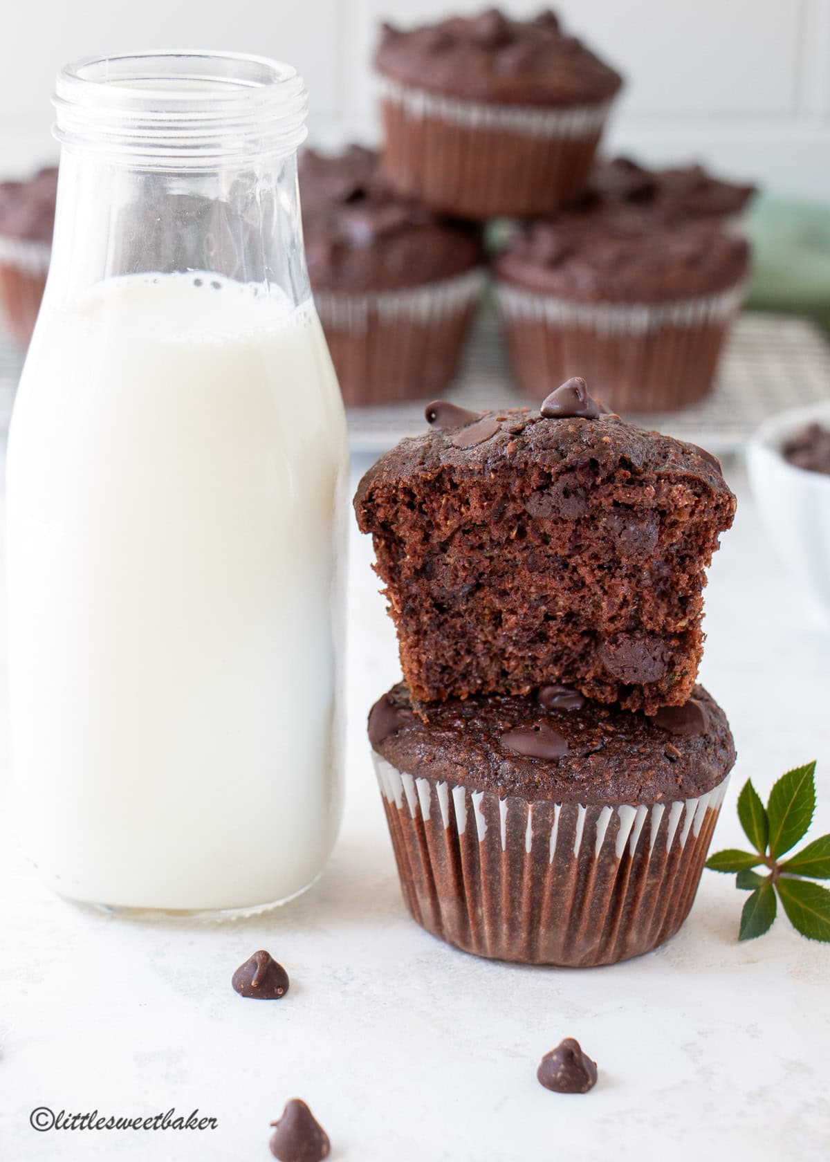 Two healthy chocolate zucchini muffins stacked with the top one broken in half and a glass of milk.