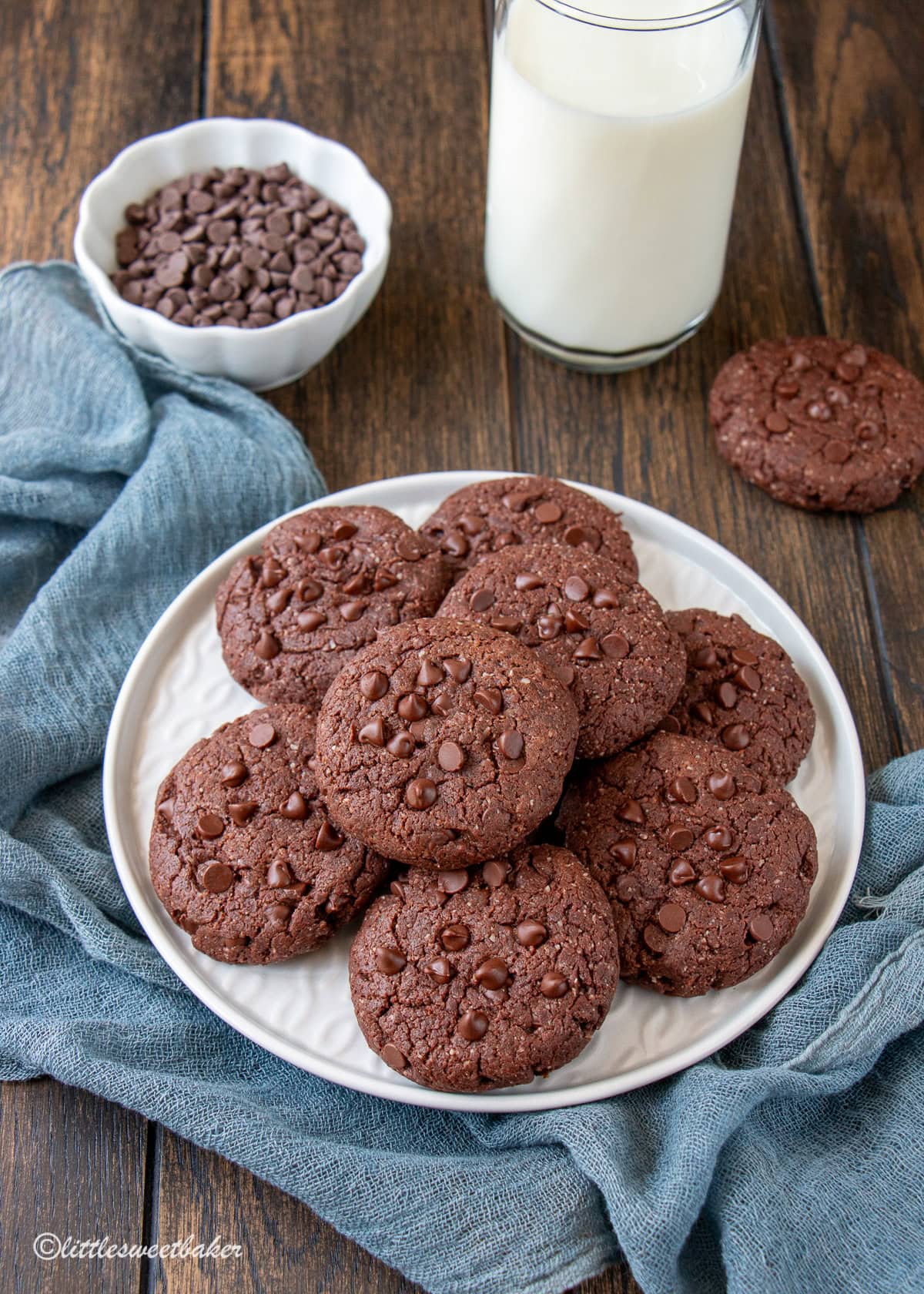 A plate of healthy double chocolate cookies on a blue chiffon napkin and glass of milk.
