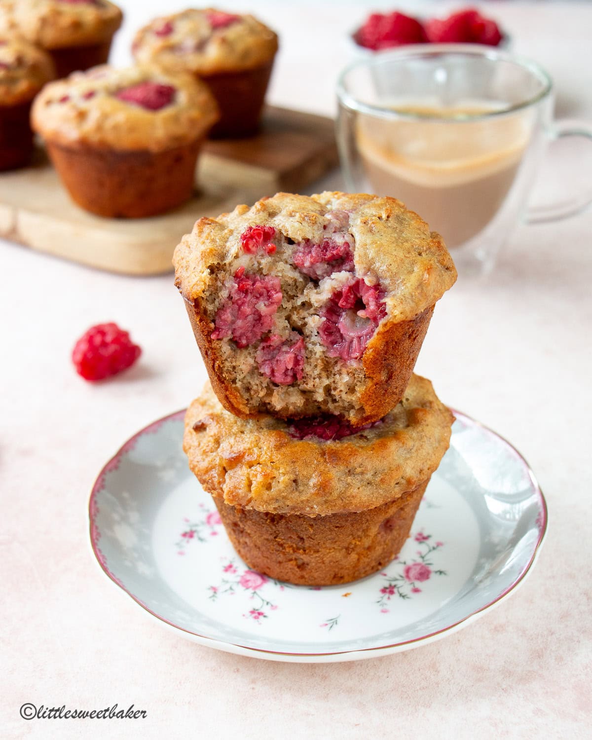 Two high-fiber raspberry bran muffins on a teacup saucer with a bite missing from the top muffin.