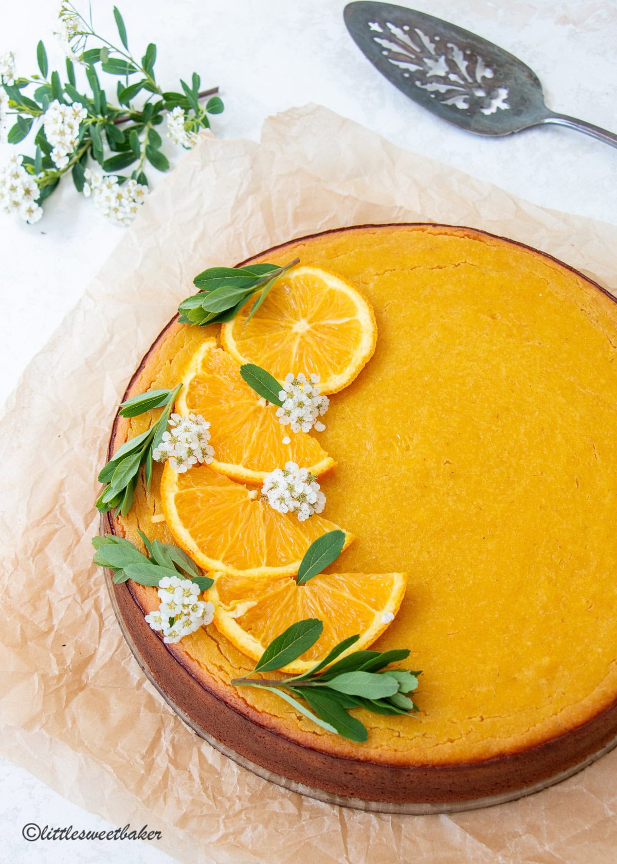 A whole orange custard cake topped with sliced oranges and white flowers.