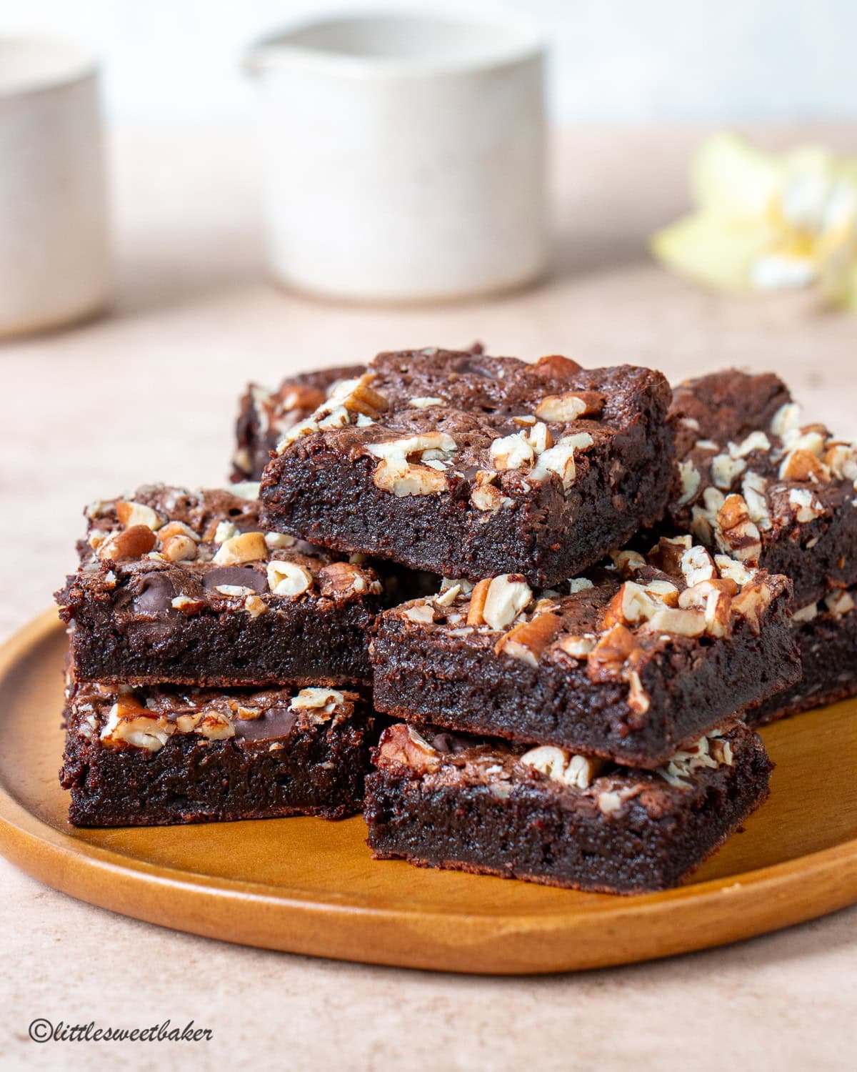 A small wooden plate of high-protein brownies topped with pecans.