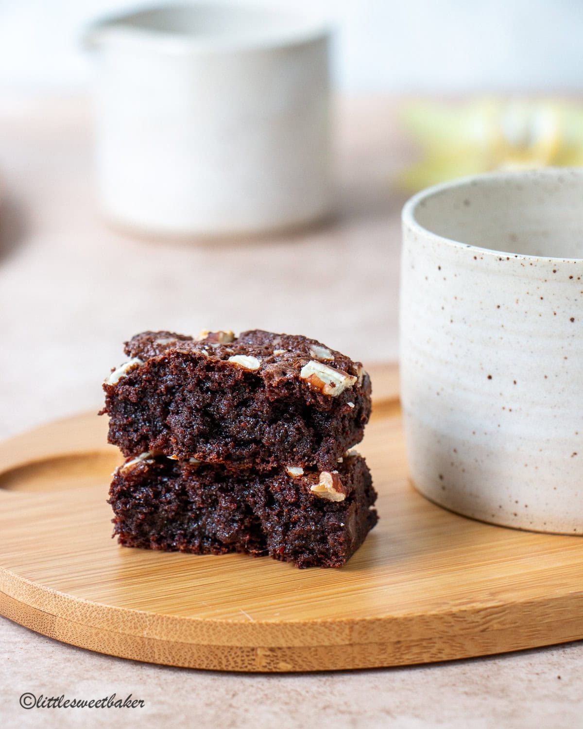 A high-protein brownie broken in half on a wooden plate with a ceramic mug.
