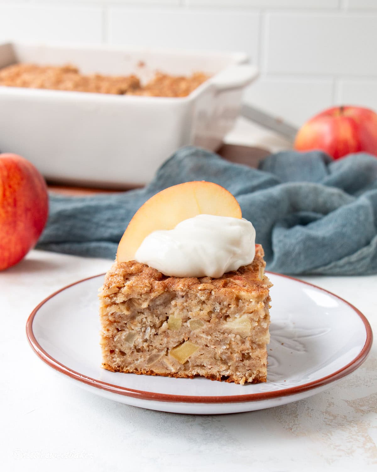 A slice of healthy apple oatmeal cake on a dessert plate topped with a dollop of yogurt and apple slice.