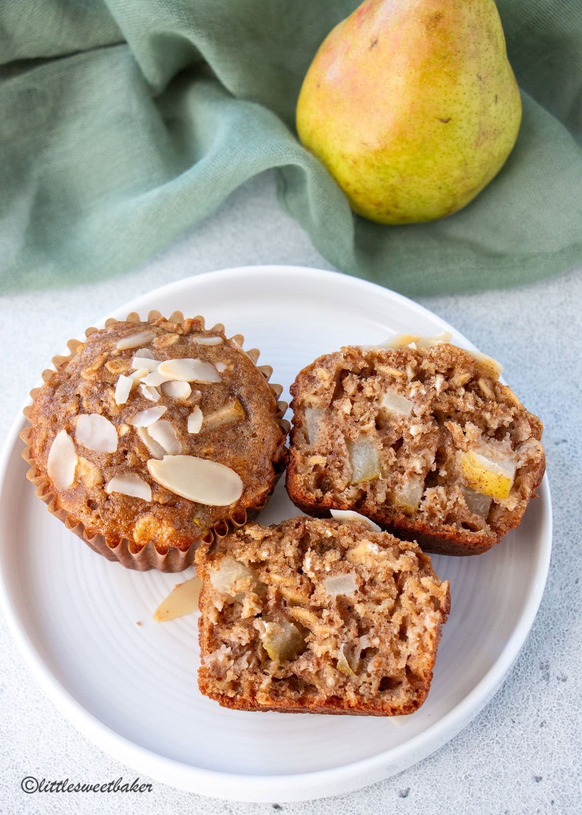 Two healthy pear muffins on a white plate, with one cut in half.
