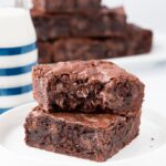 A stack of two brownies on a white plate with a bite taken out of the top one.